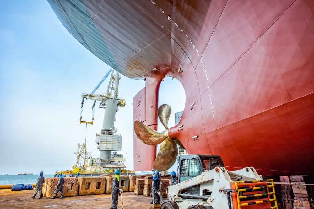 Workers beside a ship's hull and propeller in dry dock